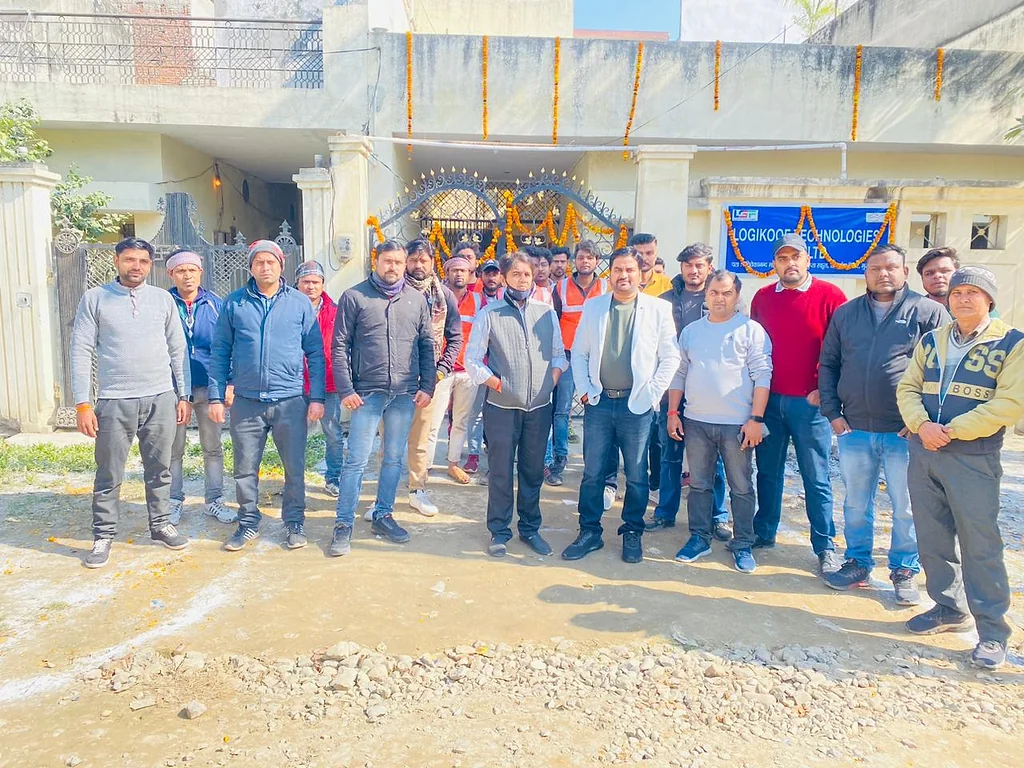 Group photo of around twenty team members standing in front of a gate decorated with marigold garlands