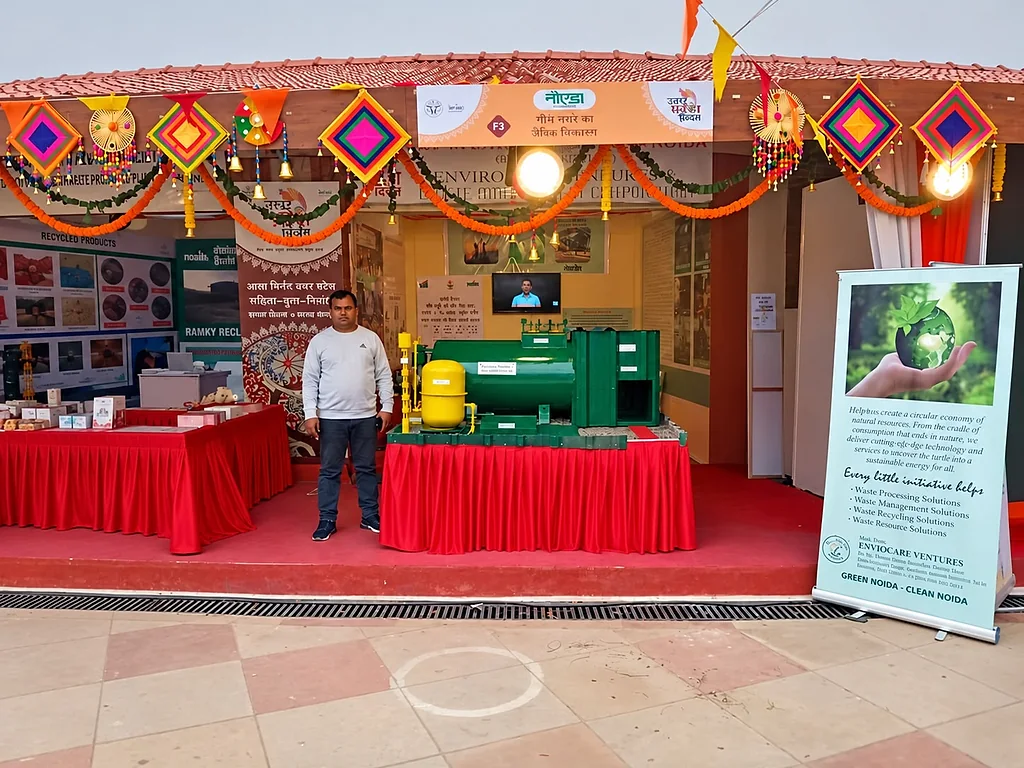 Exhibition stall at the Noida Authority pavilion during UP Diwas, with a green and yellow organic waste converter model on a red stage