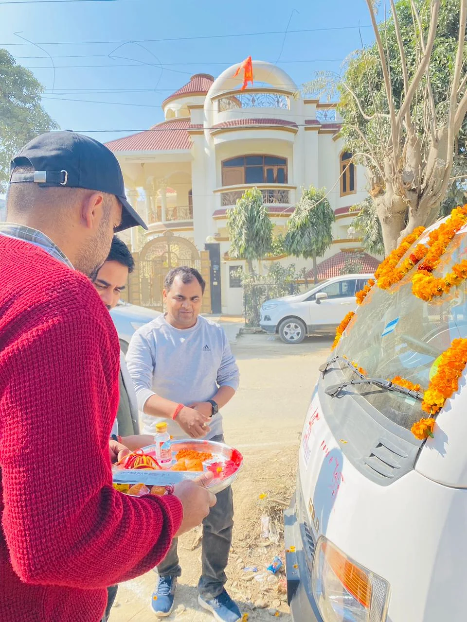 Team members holding a puja thali beside a white collection vehicle covered in marigold garlands